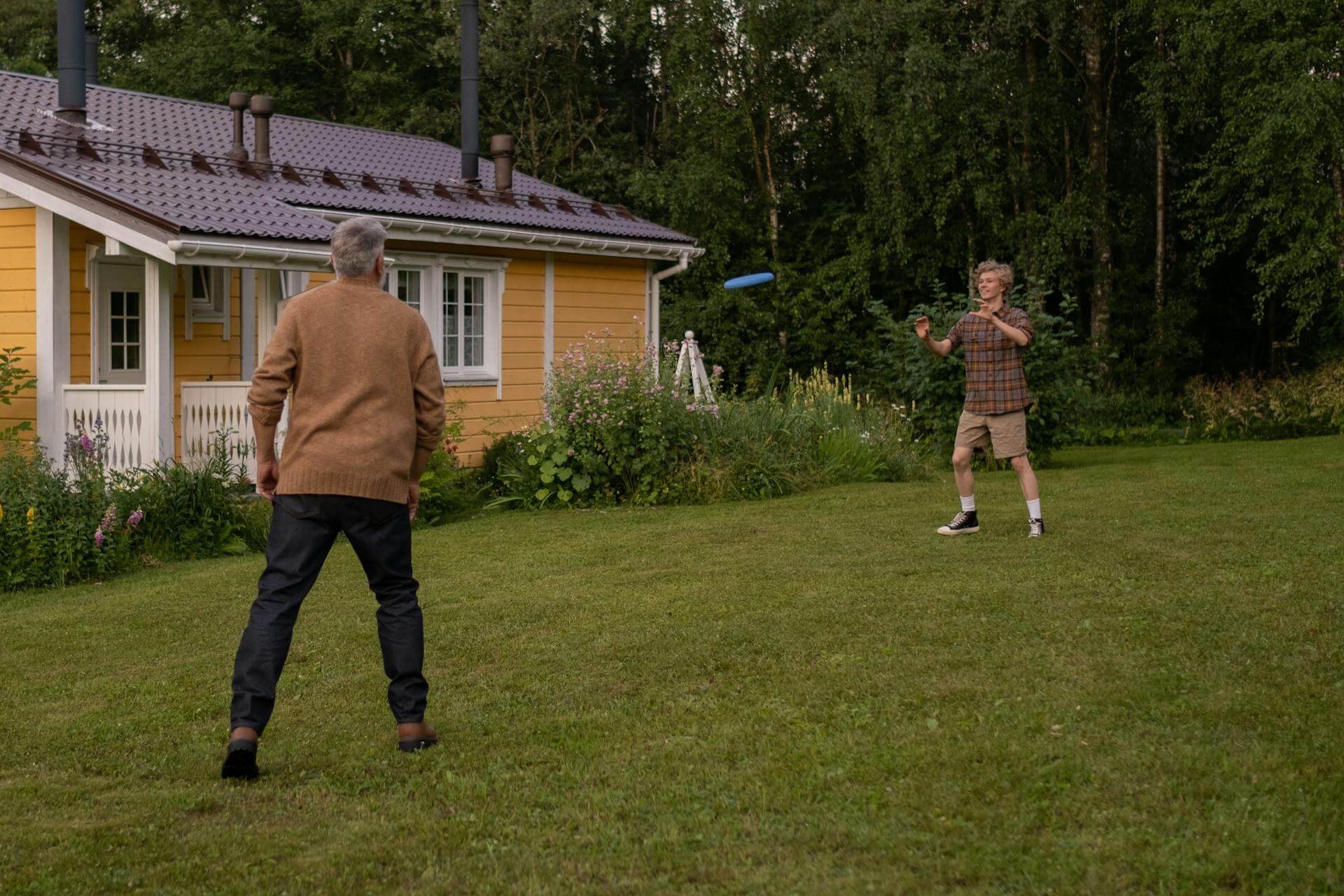 Äldre man som kastar en frisbee med sitt barnbarn på landsbygden. En GPS-klocka för äldre på landsbygden är en trygghet.